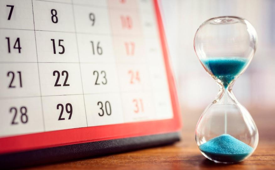 Blue hourglass and calendar on wooden table