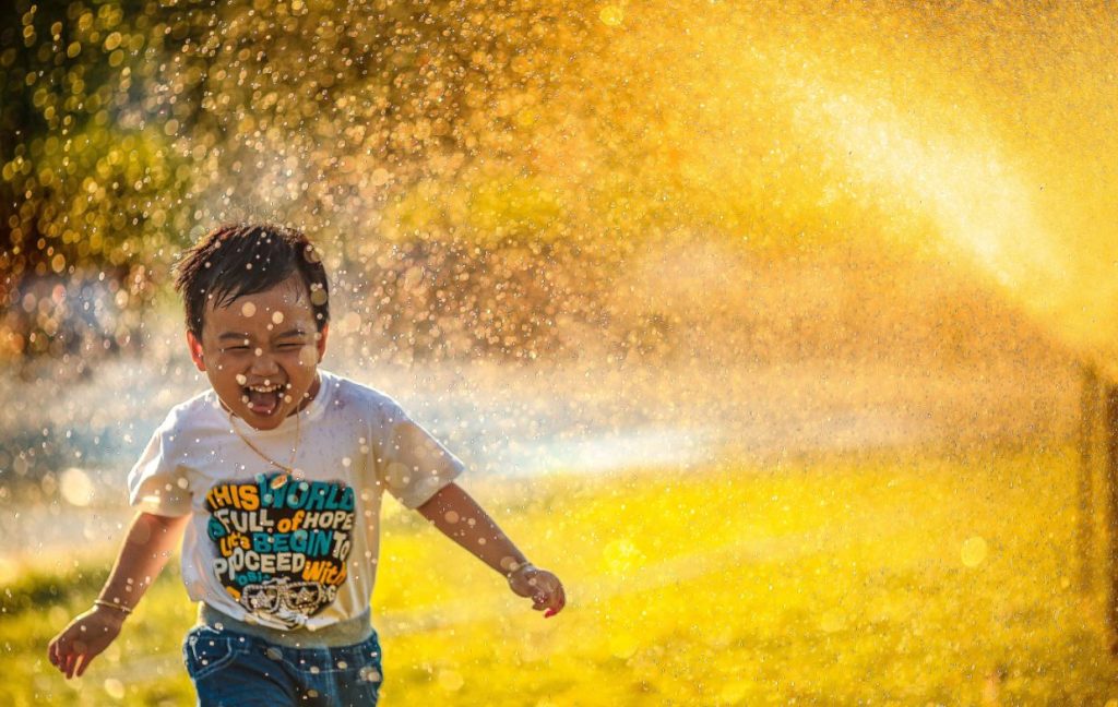 Young boy running through sprinklers laughing
