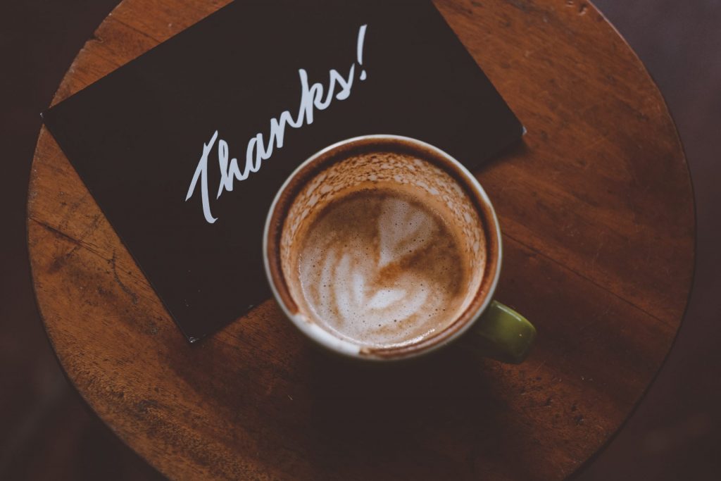 Coffee on a table next to card with thank you written on it
